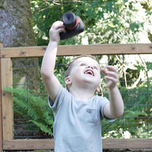 Child playing outdoors holding Mini Photographer Digital Camera in hand raising it joyfully