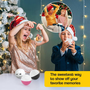 Children wearing Santa hats holding video memory Christmas tree ornaments with a holographic display of family moments inside the spheres near a decorated Christmas tree